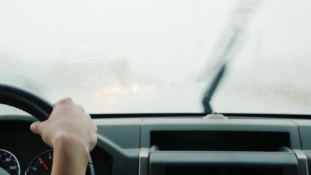 Close up view of car driver hands on steering wheel during heavy downpour driving on highway with wipers moving.