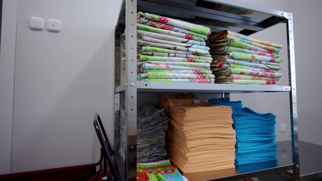 Metal shelving unit holds stacks of colorful folded towels and blankets. Large red laundry bag stands ready in corner of utility room
