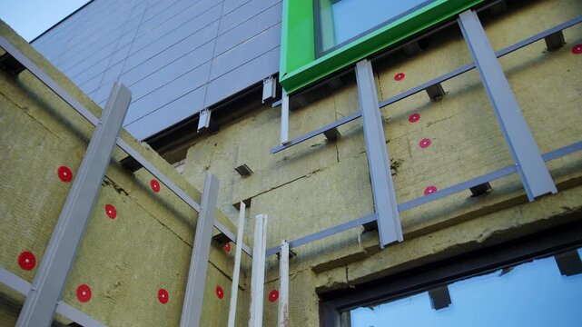 Metal grid covers mineral wool insulation on facade under window frame. Thermal panels protect building during ongoing renovation work