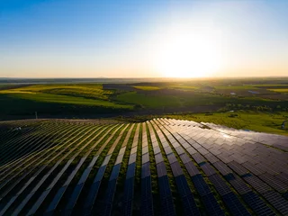 Fotobehang Beige Sunset over solar panels in a green field located in countryside, showing renewable energy in action during late afternoon  © DSMT