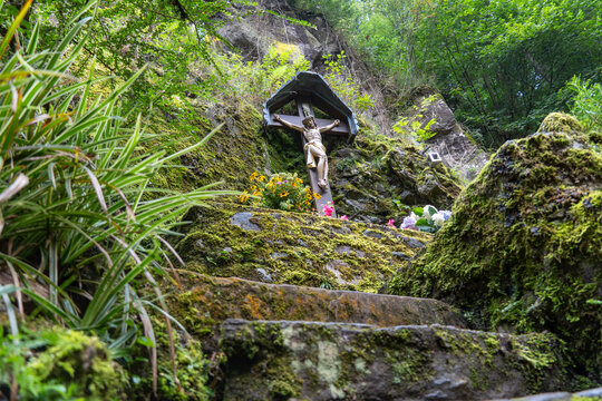 Religious wayside cross surrounded by moss covered rocks and forest vegetation in a peaceful natural mountain landscape.