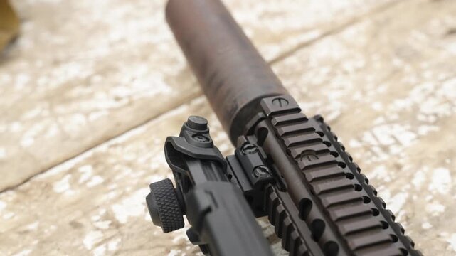 Close up of rifle fitted with suppressor showing barrel and tactical components in outdoor setting
