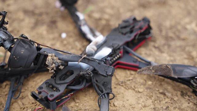 Damaged FPV drone with burnt components and broken structure on dirt ground outdoors