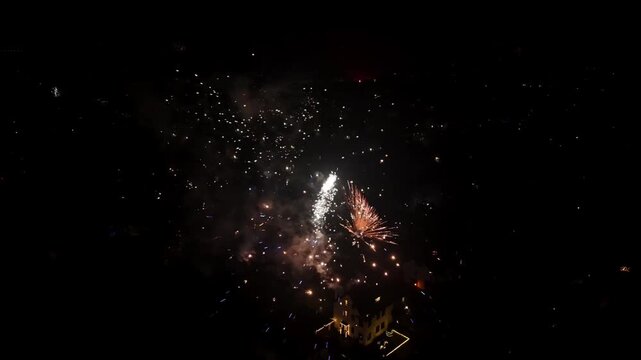 A spectacle of fireworks at night in Berlin displaying different colors and patterns at exploding, with the city behind in the dark background.