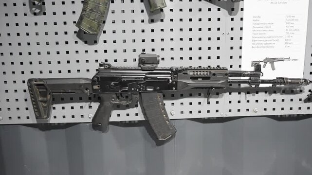 Modern assault rifle displayed on wall rack in indoor armory setting with neutral lighting