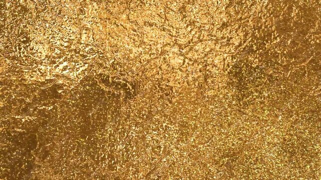 Liquid gold texture with glitter. Dynamic background of shimmering gold with glowing particles. Shimmering gold background with the effect of foil and gold leaf.