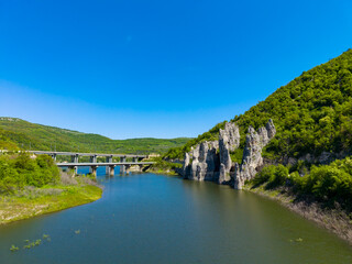 Obraz premium Landscape features a river, rocks, and a bridge in a green valley on a bright day in a rural area
