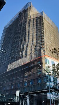 High-rise building under construction with scaffolding mesh on clear sunny day