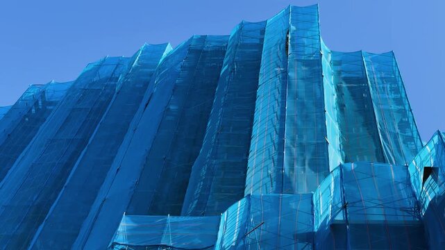 Tall building wrapped in blue construction netting under clear blue sky, renovation scene