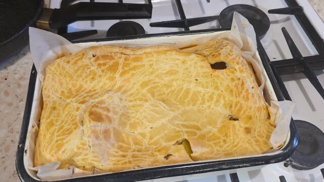 Freshly baked homemade pie in a rectangular tray on a gas stove. Golden brown crust of prepared pastry dish. Culinary process of cooling finished baked meal.