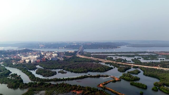 Drone shot capturing Atal Setu cutting across the wide Mandovi River, showcasing smooth traffic flow, layered waterways, and soft atmospheric haze distant landforms gradually disappearing.
