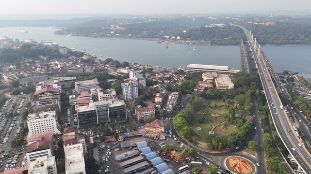 Wide cinematic aerial of a cityscape during winter capturing curved highways and busy intersections in Panaji KTC Bus Stand, Goa, leading toward Atal Setu, with river views and greenery adding depth.