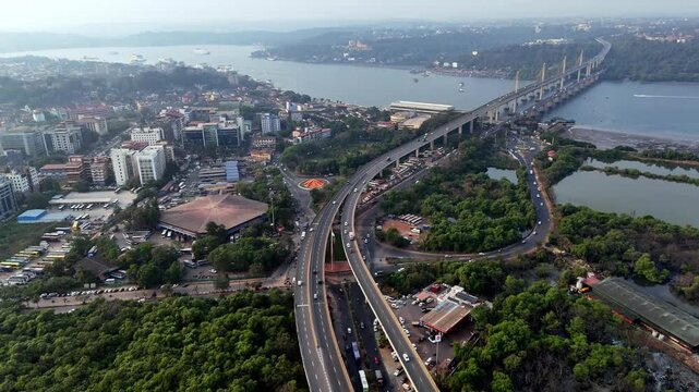 Cinematic aerial view of Panaji with sweeping flyovers merging into Atal Setu, stretching across the Mandovi River, blending urban movement with calm waterways.