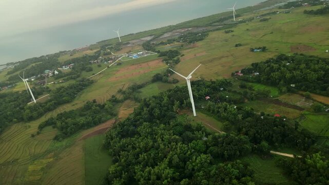Aerial flyover of wind turbines across farmland and rural landscape in Guimaras, Philippines with coastal terrain and scattered vegetation.