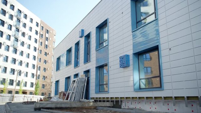 Modern building facade features window frames and decorative vents. Construction materials lean against exterior wall during final work