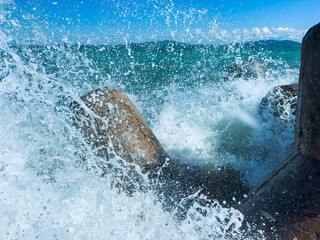 Naklejka premium Waves crash against rocks by the sea under a clear blue sky in a coastal area in daytime