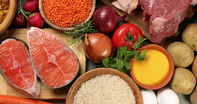 Healthy products on a gray table. Close-up footage of fish, meat, chicken, onion, radish, lettuce, mint, avocado, tomatoes, potatoes, eggs, rice, carrots, lentils, macaroni, on a rotating table.