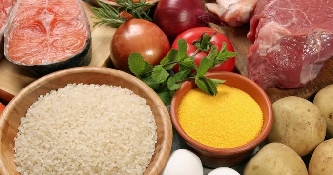 Healthy products on a gray table. Close-up footage of fish, meat, chicken, onion, radish, lettuce, mint, avocado, tomatoes, potatoes, eggs, rice, carrots, macaroni, corn porridge on a rotating table.