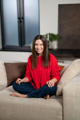 Obraz premium Pretty young woman in red sweater sitting on the sofa at home