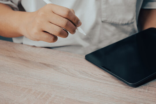 Hand Holding Stylus Pen About to Write on Black Tablet on Wooden Desk, Digital Technology Creative Concept