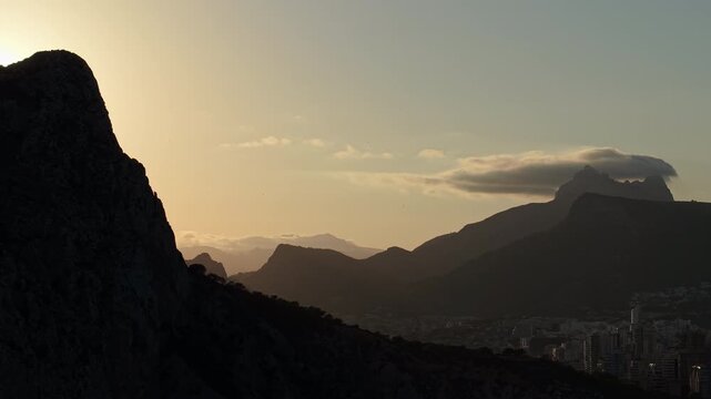 Sunrise behind Penon de Ifach with mountain silhouettes and Calpe skyline aerial landscape Spain