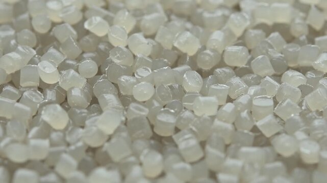 Translucent plastic pellets slowly rotate in macro view as industrial polymer raw material for production background loop