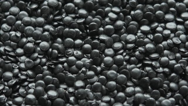 Close view of rotating black polyethylene granules creates dense plastic texture for industrial processing and recycling