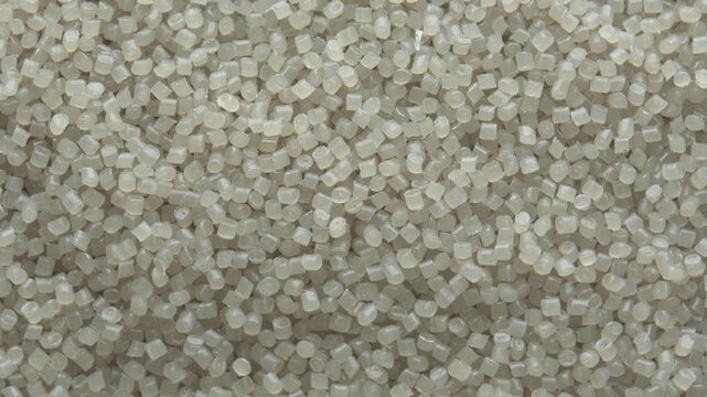 Top view of translucent plastic pellets rotating slowly, creating industrial polymer texture for manufacturing background