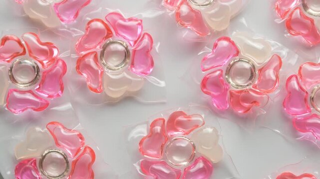 Pink flower shaped laundry detergent pods rotate on white background in top view as household cleaning product concept loop