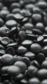 Vertical close up of black polyethylene granules in slow rotation creates texture for recycling and industrial production