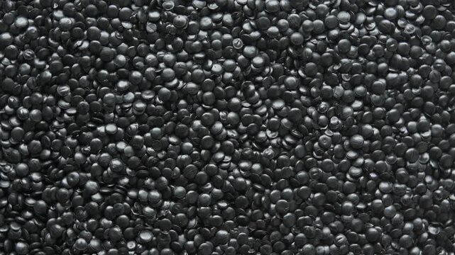 Top view of rotating black polyethylene granules forms dense plastic texture for recycling and industrial processing needs