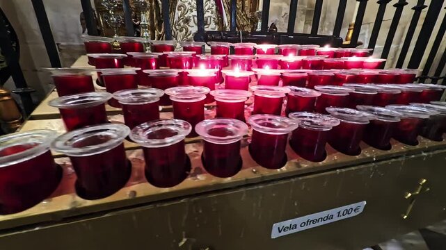 Rows of red votive candles in plastic cups burn on a church altar, offered as donations for prayer and devotion.