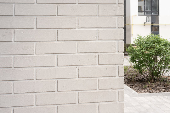 Light grey painted brick wall texture creating a modern architectural facade with building and plant background