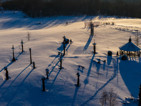 Aerial view of the Hill of Angels featuring wooden sculptures and a gazebo with long shadows on the snow-covered field during sunset in Traku rajonas, Vilniaus apskritis, Lithuania.