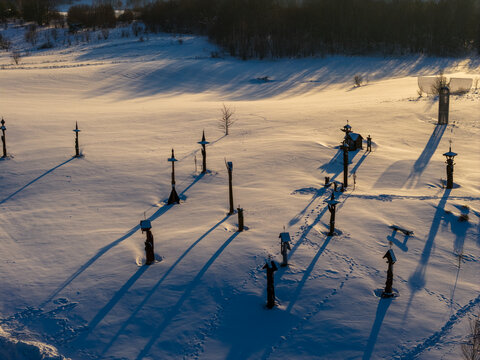 Aerial view of the Hill of Angels featuring tall wooden sculptures and long shadows across a snow-covered field in Traku rajonas, Vilniaus apskritis, Lithuania.