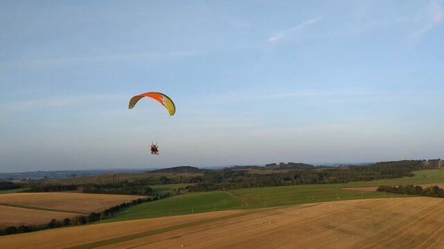Aerial panorama of paragliding pilot with paramotor flying midair above landscape