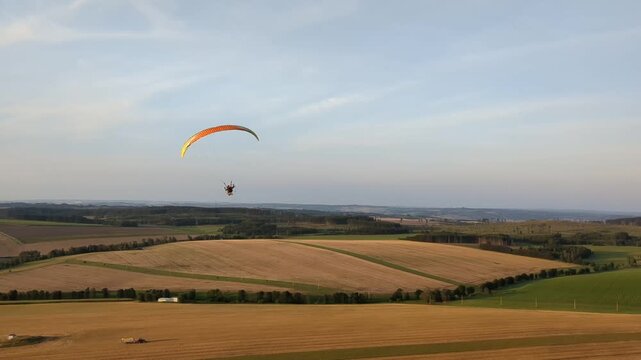 Aerial panorama of paragliding pilot with paramotor flying midair above landscape