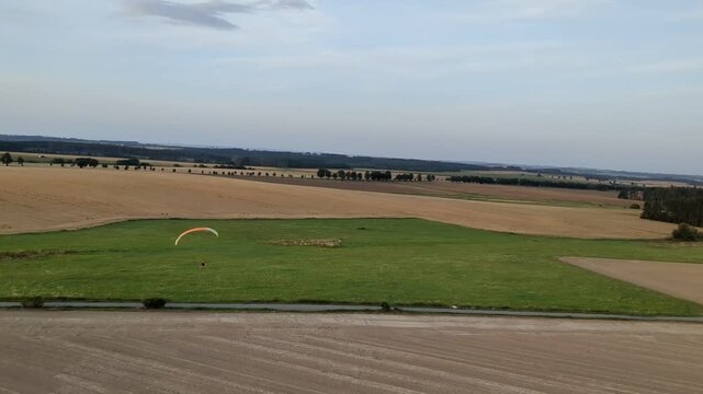 Aerial panorama of paragliding pilot with paramotor flying midair above landscape