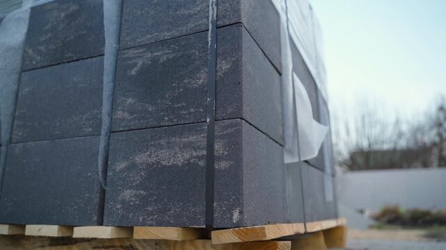 Pallet of grey concrete paving stones wrapped in plastic film. Stacked paving blocks for landscaping and construction on wooden pallet