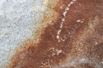 Close-up of a stone surface reveals a striking contrast between a pristine, speckled granite area and a rust-stained section with rough, earthy tones. The interplay of textures and colors evokes a sen © Semiglass