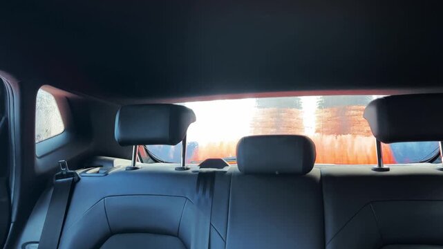 Inside a car, orange brushes rotate against the rear window, removing water and grime. Useful for automotive ads or cleaning service promotions.