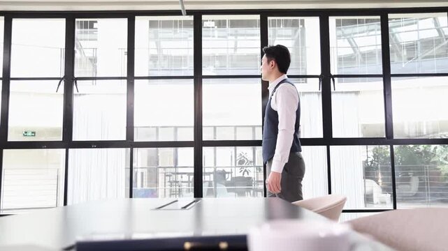 Confident businessman looks into the distance thoughtfully in a modern meeting board room office environment with laptop computer, coffee cup, thinking idea or solution while walking and forth
