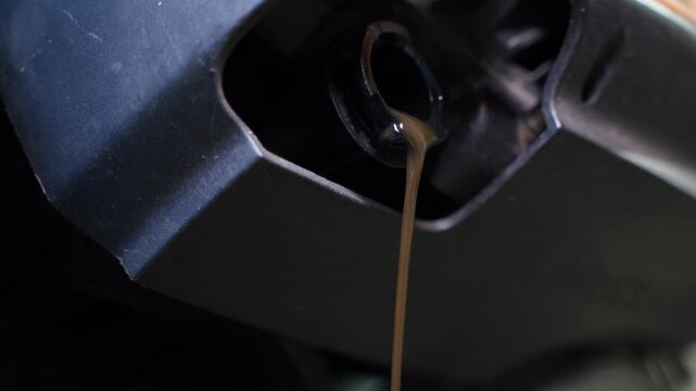 Close up of draining used motor oil from lawn mower engine. Black waste oil pouring out during garden equipment maintenance