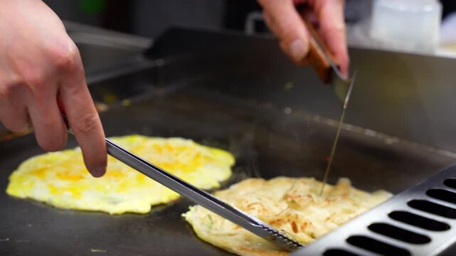 Professional chef preparing traditional Taiwanese scallion pancakes and eggs on a hot griddle
