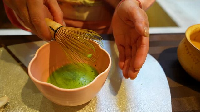 Woman's hands whipping green matcha tea in a pink bowl during a traditional Japanese tea ceremony