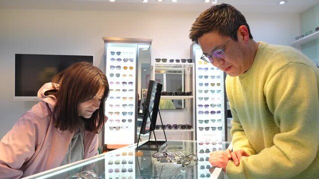 Asian man assists a young Caucasian woman in selecting a new pair of eyeglasses at an optical shop