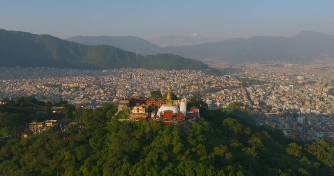 Drone shot of Swayambhu nath monkey temple stupa in Kathmandu Nepal during golden hour over green forest and valley skyline highlighting heritage architecture at UNESCO heritage site