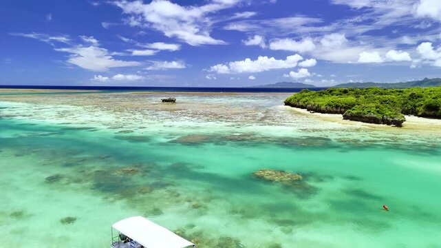 Aerial view of a white tourist boat floating on transparent turquoise water near a lush tropical islet in Kabira Bay.