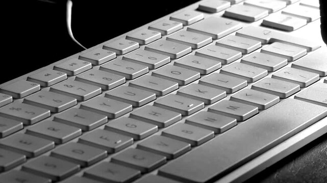 Closeup of a finger in silhouette entering a number, letter, character password on a white computer keyboard.