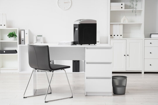 Modern shredder with documents on desk in office interior